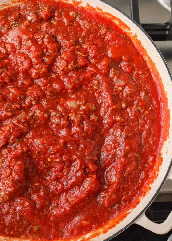 a top down photo of the right half of a white skillet with a white handle visible, inside the skillet is vivid red spaghetti sauce with meat