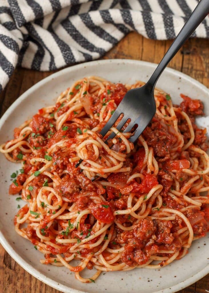 Black metal fork with bite size spaghetti coated in meat sauce