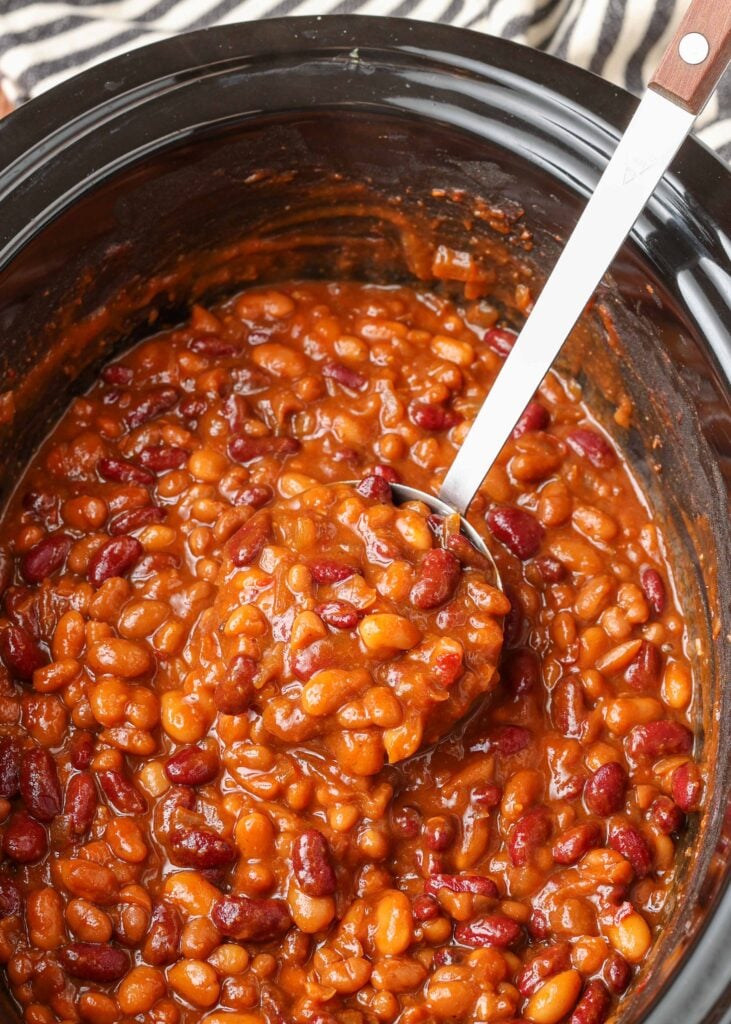 a crockput full of spicy baked beans ready to be served with a metal ladle