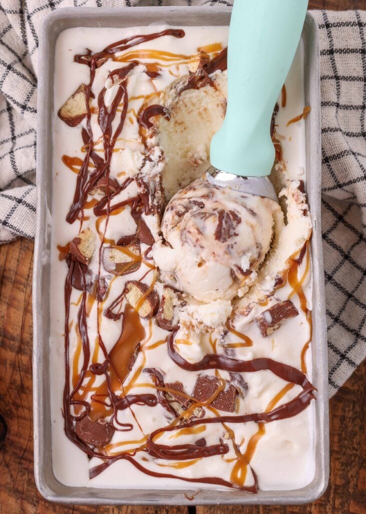 Una pallina di gelato con manico ciano è appoggiata sopra la teglia piena di gelato pronta da servire, contiene già una pallina di gelato