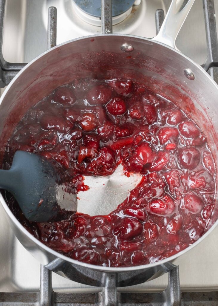 a top down photo of cherries simmering in a metal pot on the stovetop