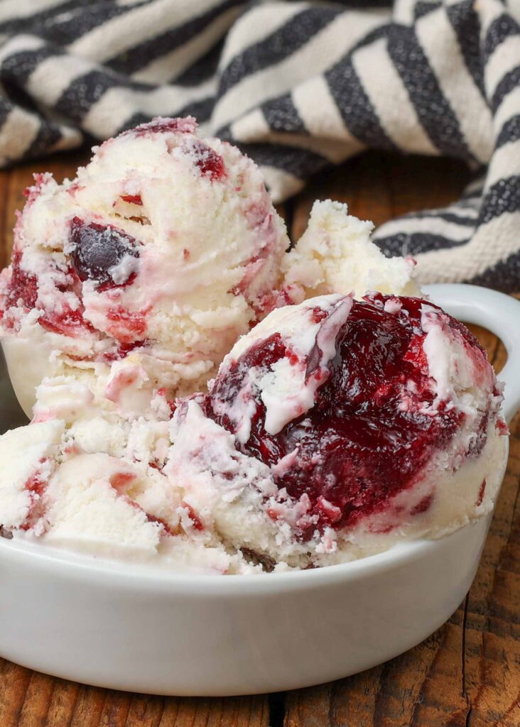 scoops of black cherry ice cream fill a white bowl on a wooden tabletop