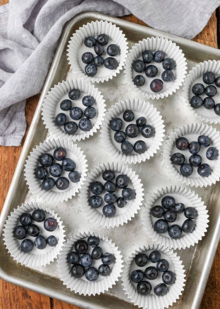 Blueberries in small clusters on a silver tray with white cupcake wrappers
