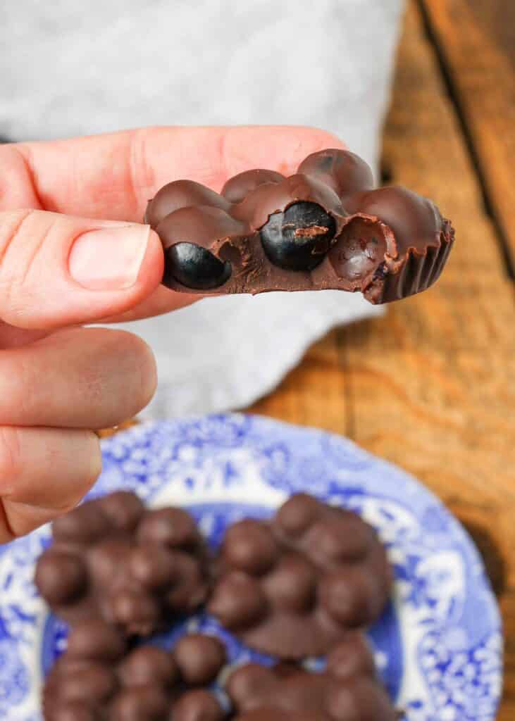 A woman's hand holds a chocolate covered cluster of blueberries. A bite has been taken out of the cluster
