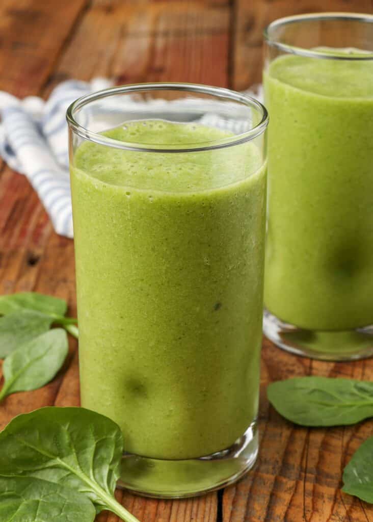 a tall glass of a banana spinach smoothie stands on a wooden tabletop