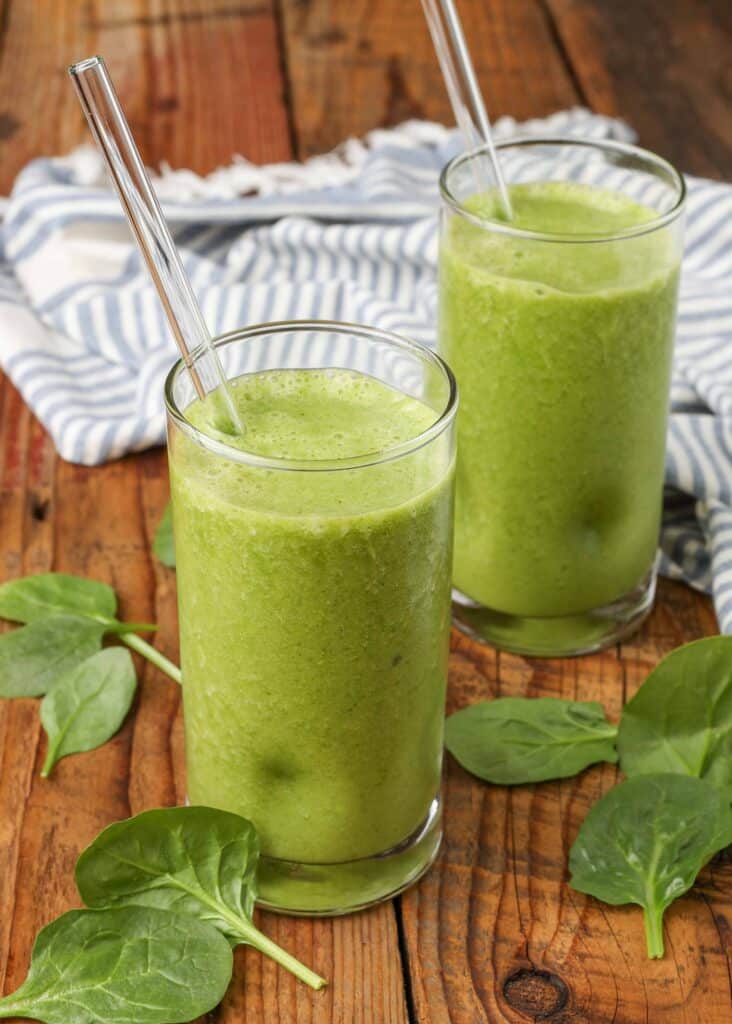 two tall glasses full of spinach smoothies with a blue and white striped tea towel in the background
