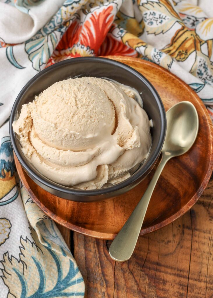 a metal spoon rests on the wooden plate beside a small grey bowl with a scoop of ice cream in it
