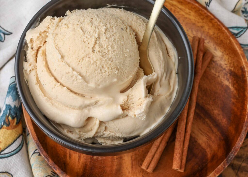a scoop of chai ice cream in a bowl on a wooden plate with sticks of cinnamon visible in the background