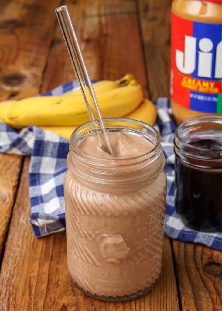 a mason jar full of peanut butter chocolate smoothie with the ingredients visible in the background