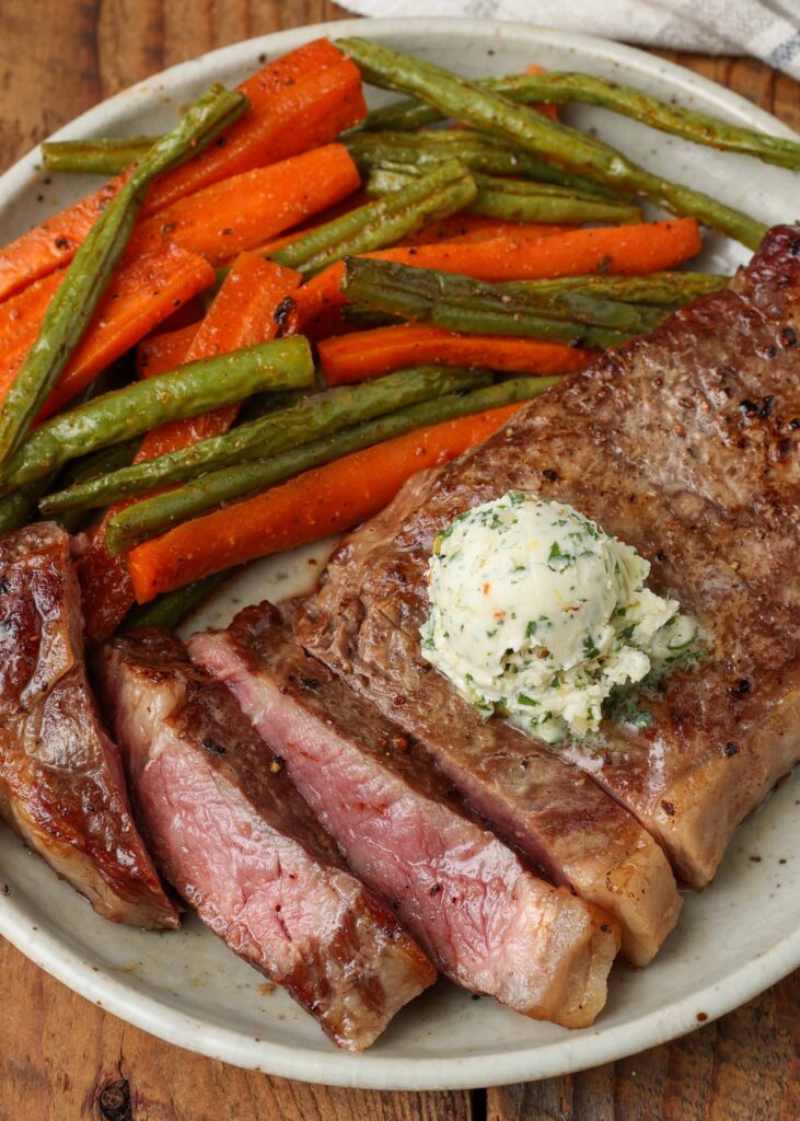 sliced steak topped with garlic herb butter on plate with vegetables