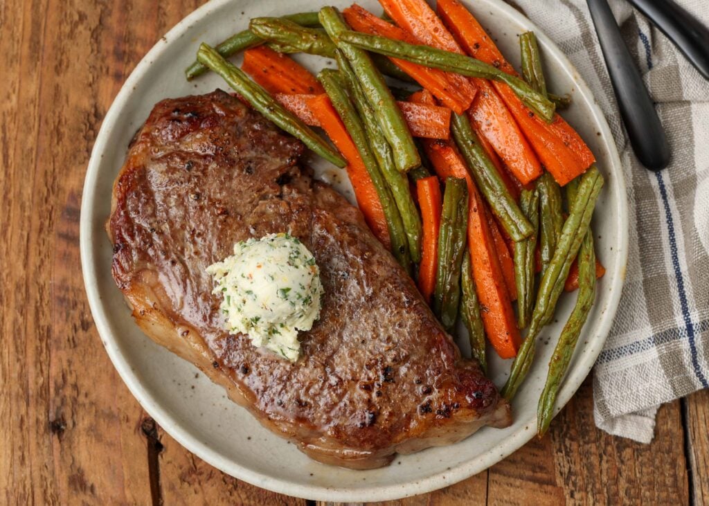 steak resting on plate next to carrots and green beans