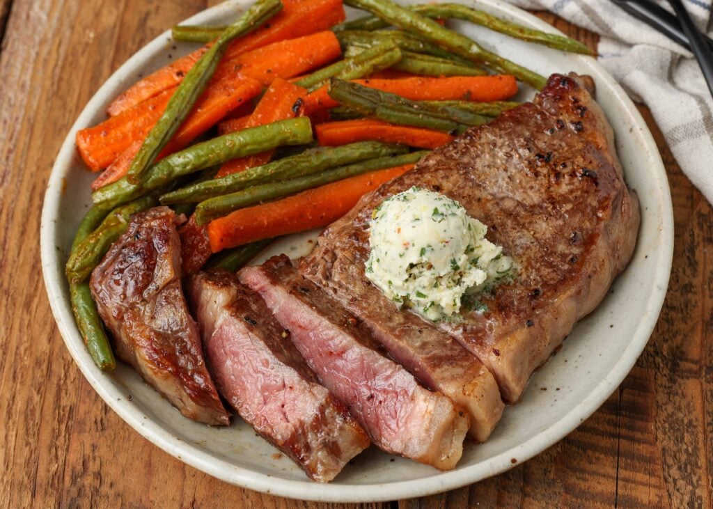 sliced steak on plate next to green beans and carrots