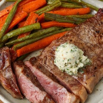 sliced steak on pottery plate, topped with butter, next to vegetables