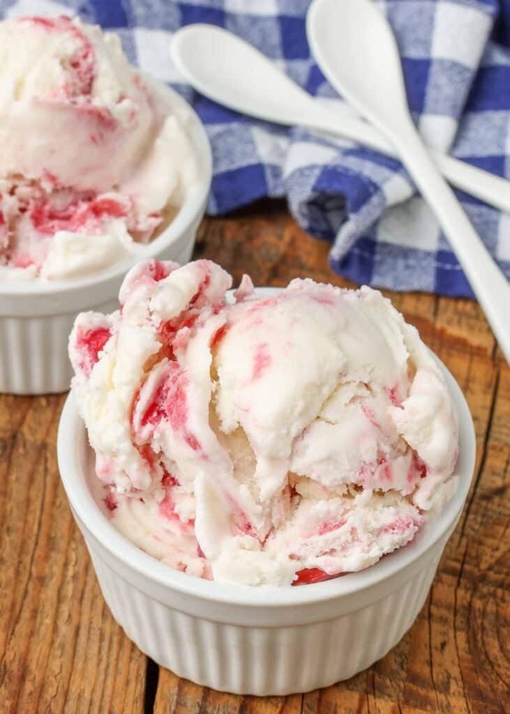  white and red rhubarb swirl ice cream, served in a white bowl with a silver spoon and a checkered blue and white towel