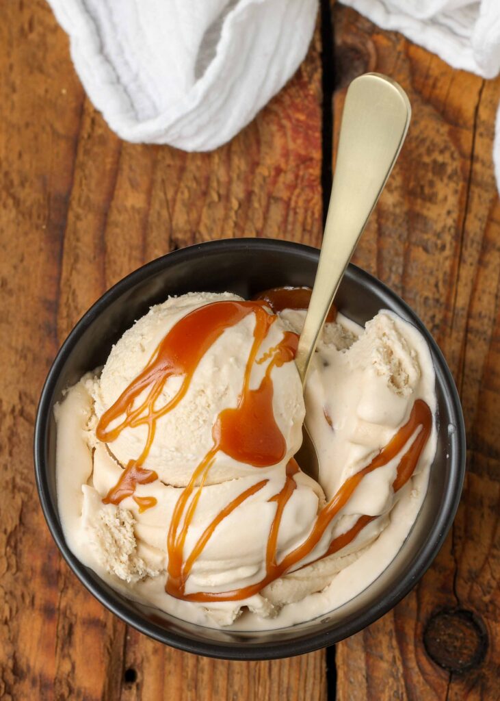 Salted Caramel Ice Cream in small bowl with spoon on wooden table with white linen
