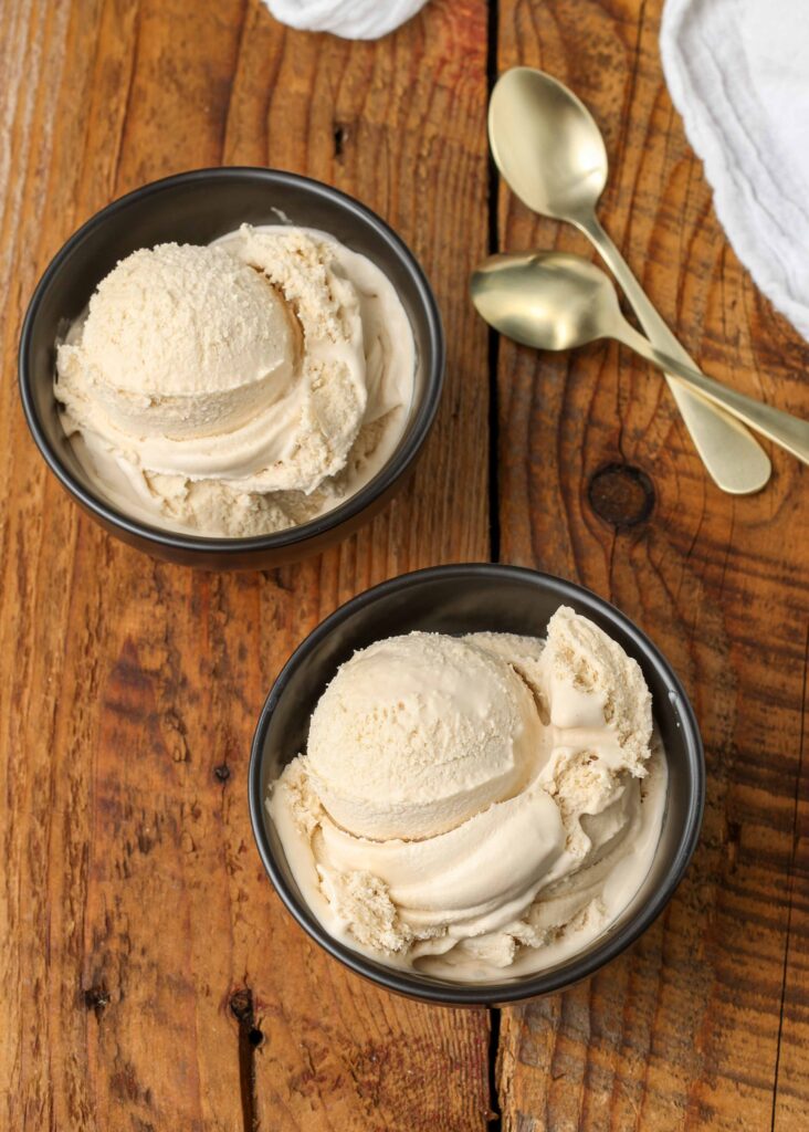 Caramel ice cream served in black bowls with gold spoons on a wooden table