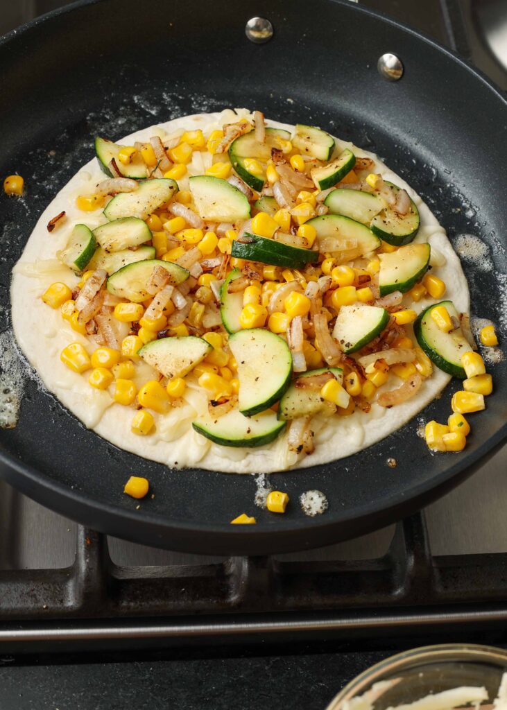 Overhead shot of quesadilla in skillet in the middle of cooking, with cheese, corn, and zucchini piled onto a tortilla