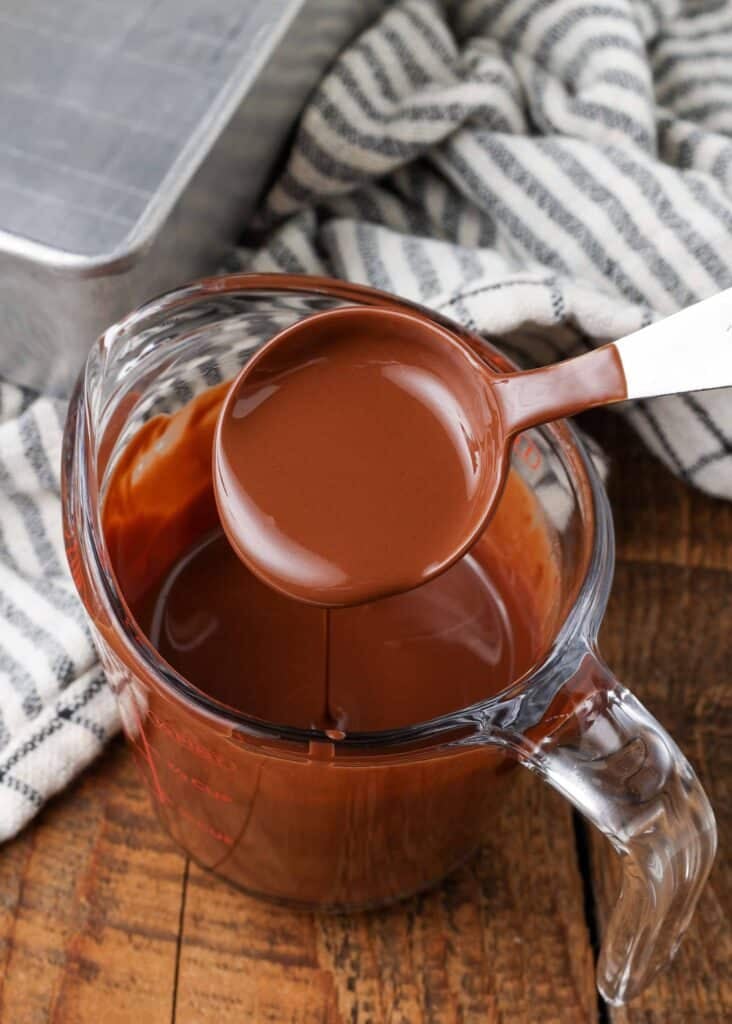 Overhead shot of melted chocolate being scooped from a glass bowl by a quarter cup measure