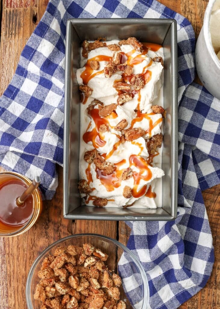 Overhead shot of pralines and cream ice cream topped with caramel syrup and pralines, served in a long silver tray