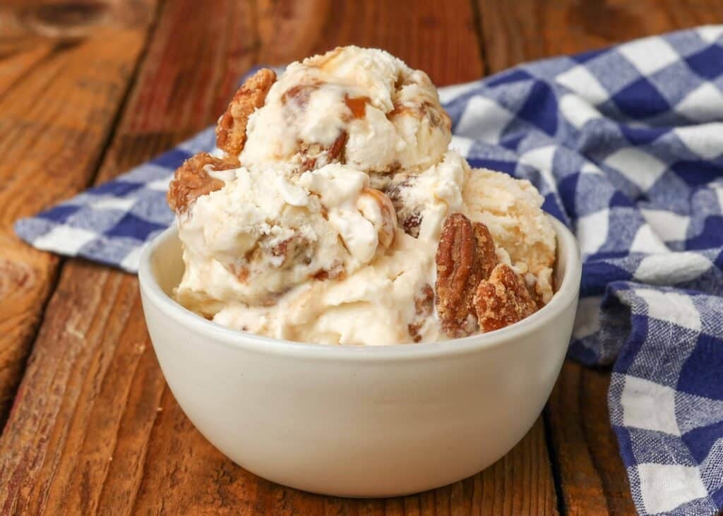 Vertical shot of pralines and cream ice cream, served in a small white bowl with a checkered blue and white towel