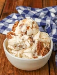 Overhead shot of pralines and cream ice cream topped with pecans, served in a small white bowl with a checkered blue and white towel