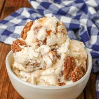 Overhead shot of pralines and cream ice cream topped with pecans, served in a small white bowl with a checkered blue and white towel