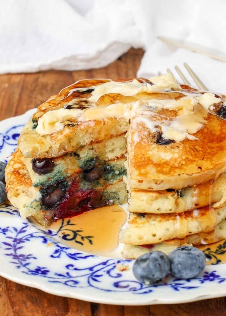 A wedge has been sliced from this stack of pancakes on a undecorous and white plate, revealing the blueberries within.