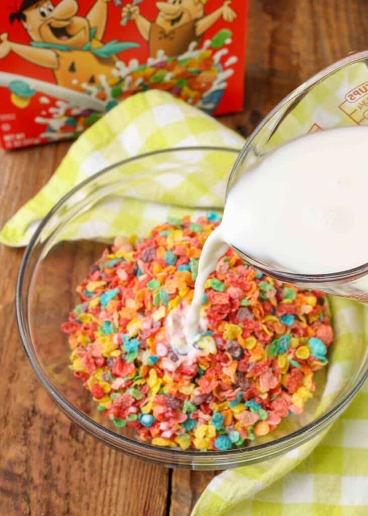Overhead shot of pouring milk into a glass trencher filled with Fruity Pebbles cereal