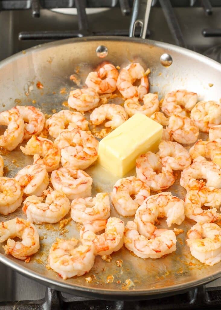 Overhead shot of butter, shrimp, and garlic cooking in a stainless steel skillet