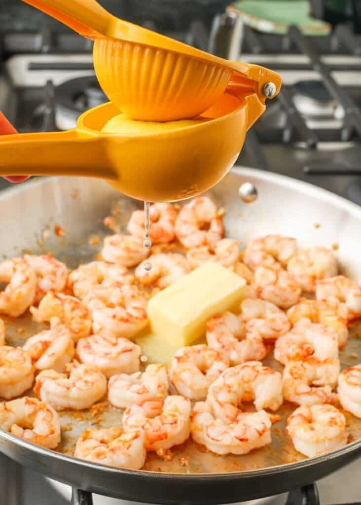 Overhead shot of lemon juicer squeezing juice onto skillet of shrimp, butter, and garlic