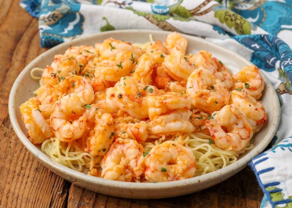Horizontal shot of garlic butter shrimp and buttery pasta, served in a white bowl with a blue and white floral pattern towel