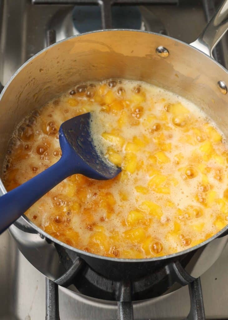 Overhead shot of peach sauce cooking in a stainless steel pan, with a blue rubber spatula