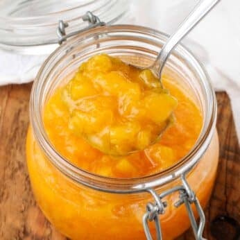 Overhead shot of peach sauce in a glass jar, served with a silver spoon