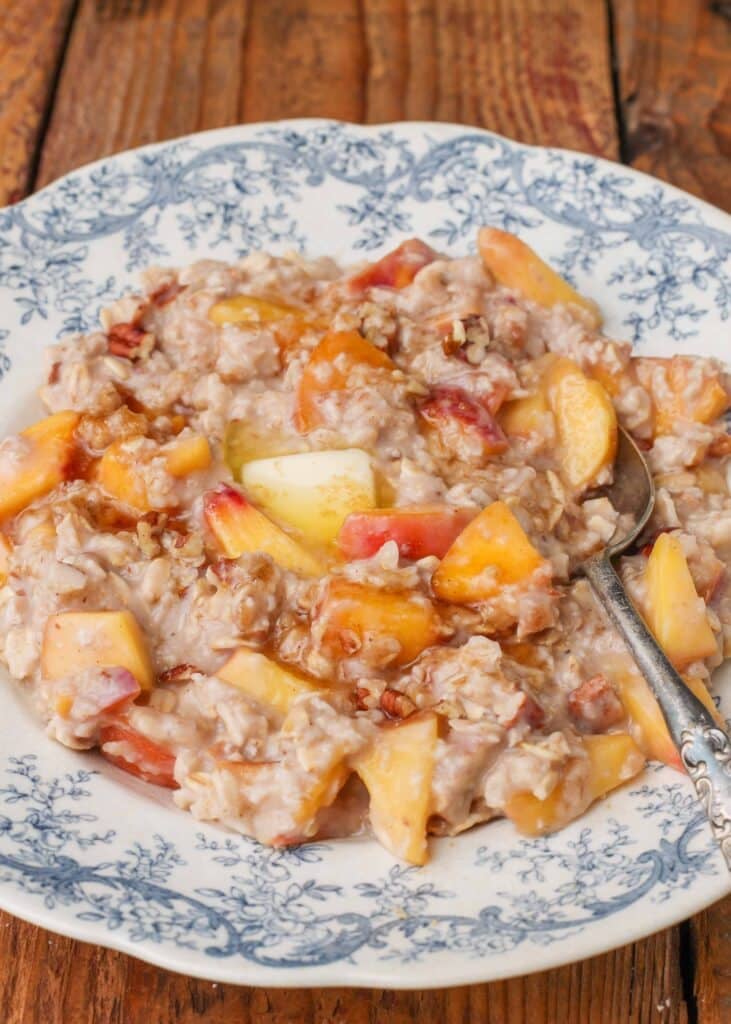 oatmeal with peaches, pecans, butter, and brown sugar in blue bowl