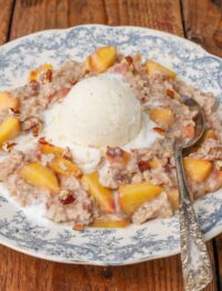 close up photo of oatmeal with peaches, pecans, and a scoop of ice cream on top