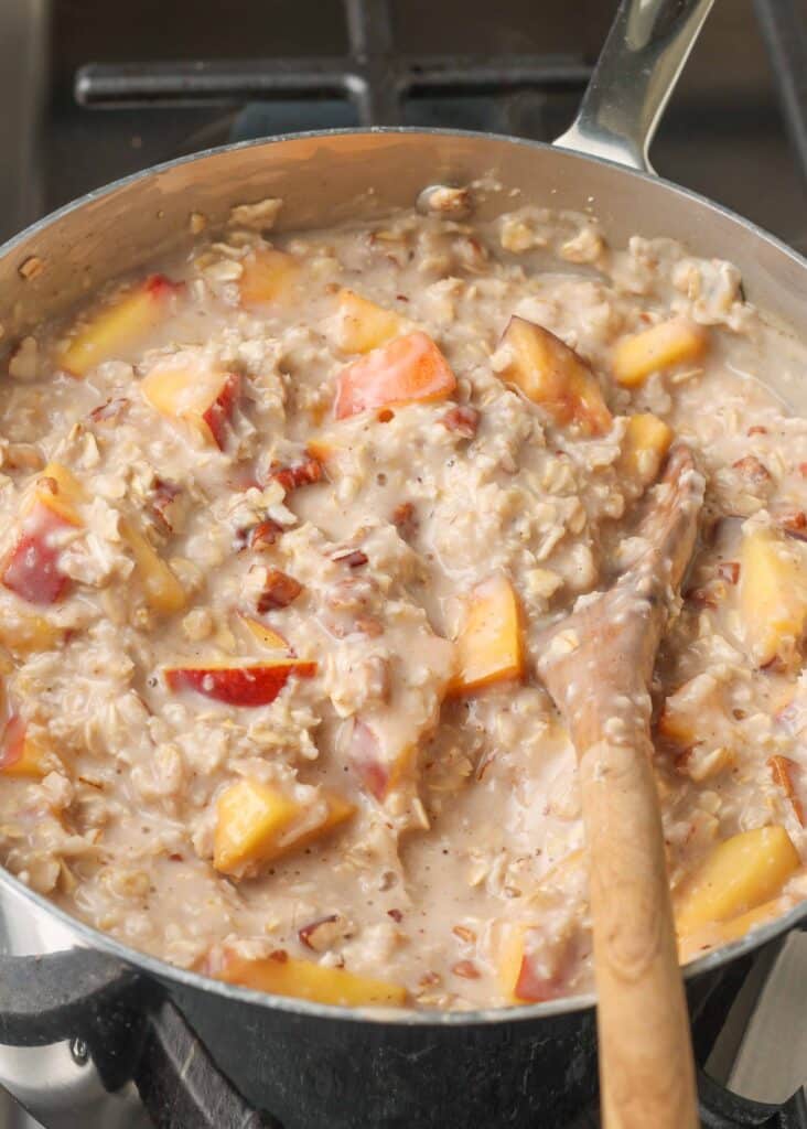 oatmeal with peaches in pan with wooden spoon