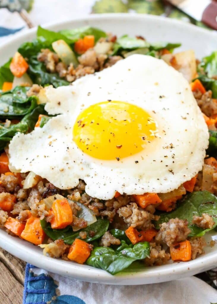 Overhead shot of Sweet Potato Hash with Eggs, topped with a sunny side up egg, served in a white bowl