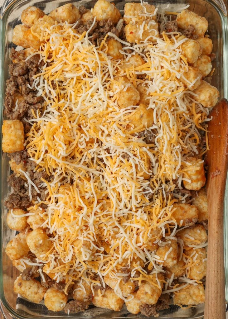 Shredded cheese has been placed atop the tater tots and crumbled sausage.