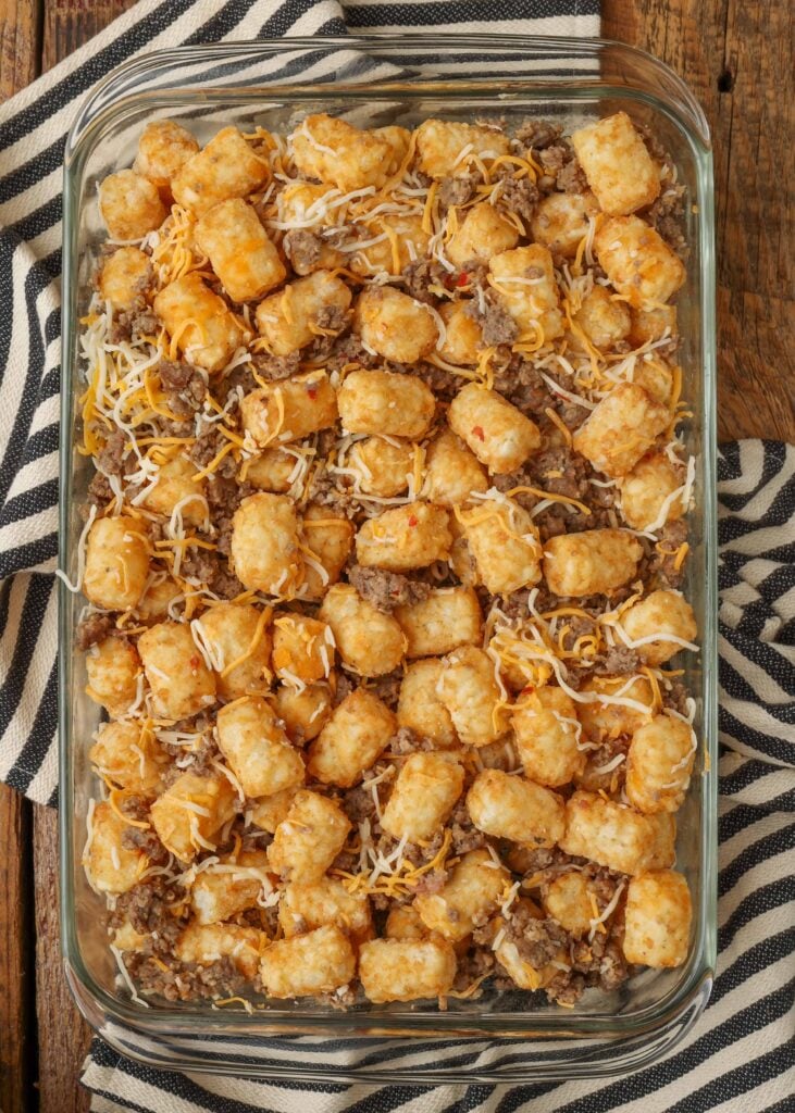 Sausage crumbles are visible in the tater tots and cheese in this clear glass baking dish.