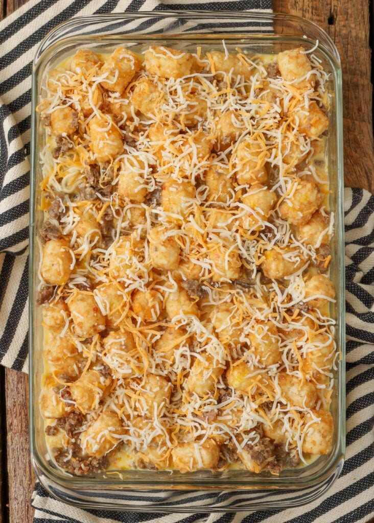 The final layer has been added to the tater tot casserole and it is ready to go into the oven in a clear glass baking dish.