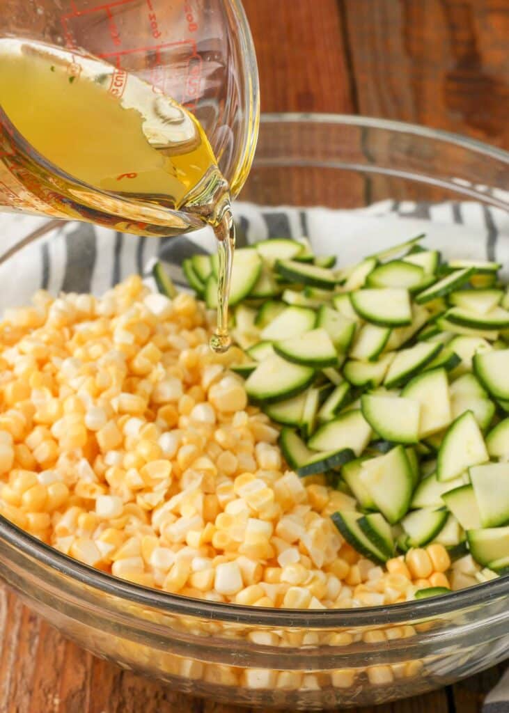 Closeup of dressing being poured into a glass bowl filled with corn and thinly chopped zucchini