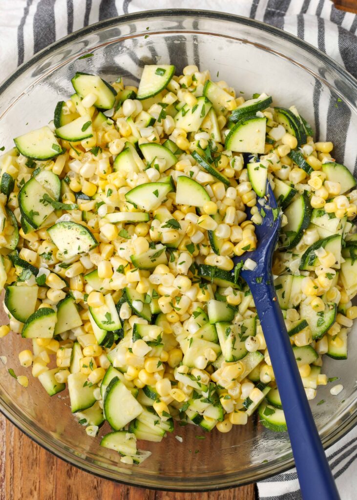 Overhead shot of zucchini corn salad in glass trencher with undecorous spatula