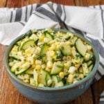 Zucchini corn salad, served in a small blue ceramic bowl with a striped gray and white towel
