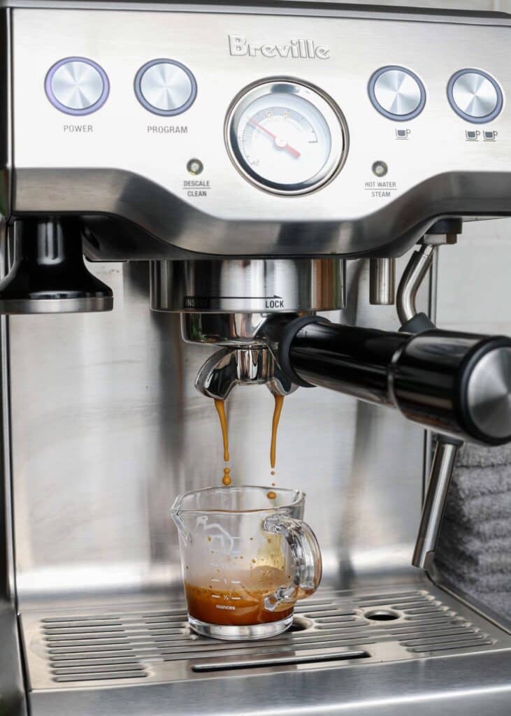 A shot of espresso pouring from a machine into a glass mug