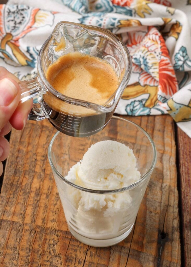 Vertical shot of glass pitcher containing espresso, poised over glass of vanilla ice cream