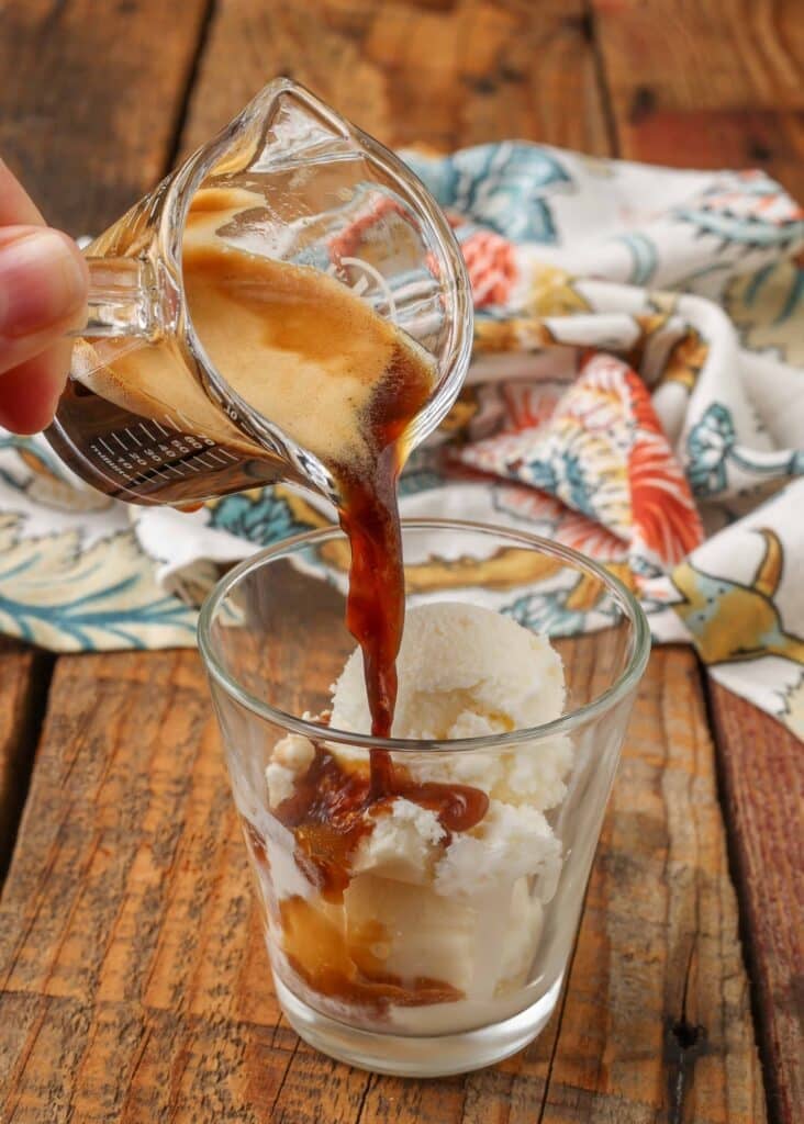 Vertical shot of espresso mid-pour, starting to cover vanilla ice cream in glass