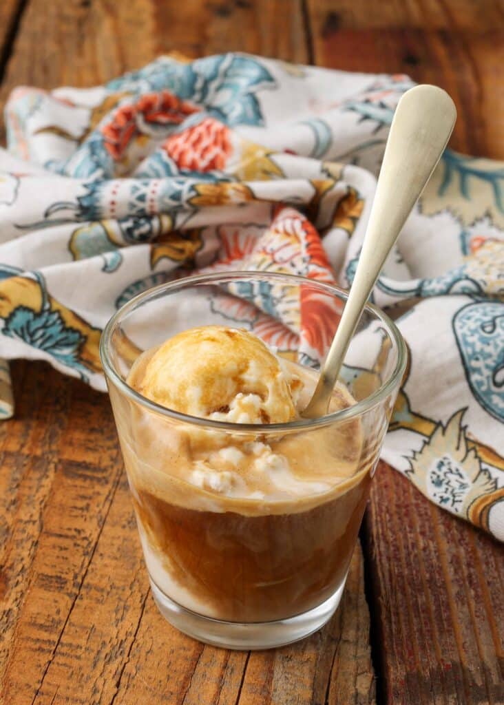 Vertical shot of affogato (vanilla ice cream and espresso) swirled together in a glass, served with a silver spoon
