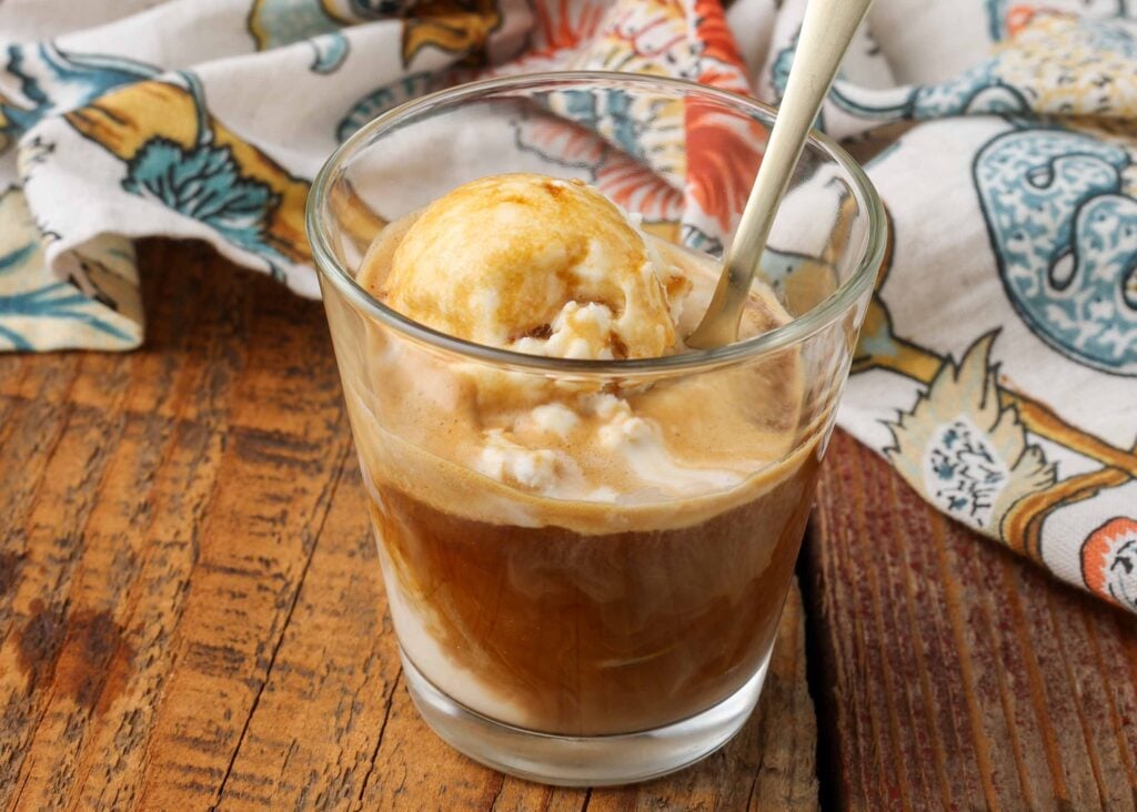Horizontal shot of affogato (vanilla ice cream and espresso), served in a glass with a silver spoon and a floral print towel