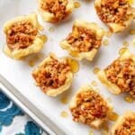 miniature baklava bites made with puff pastry on parchment lined tray next to floral napkin
