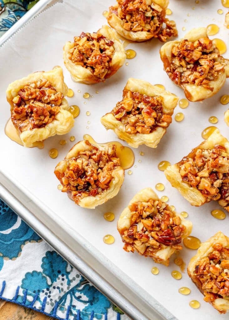 miniature baklava bites made with puff pastry on parchment lined tray next to floral napkin